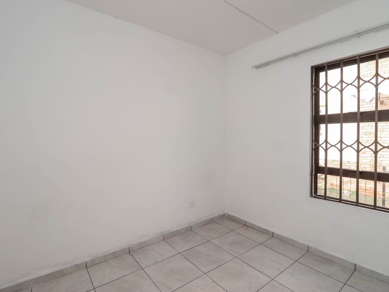 An empty bedroom featuring neutral tiled flooring, a window with a security gate, and a curtain rail.