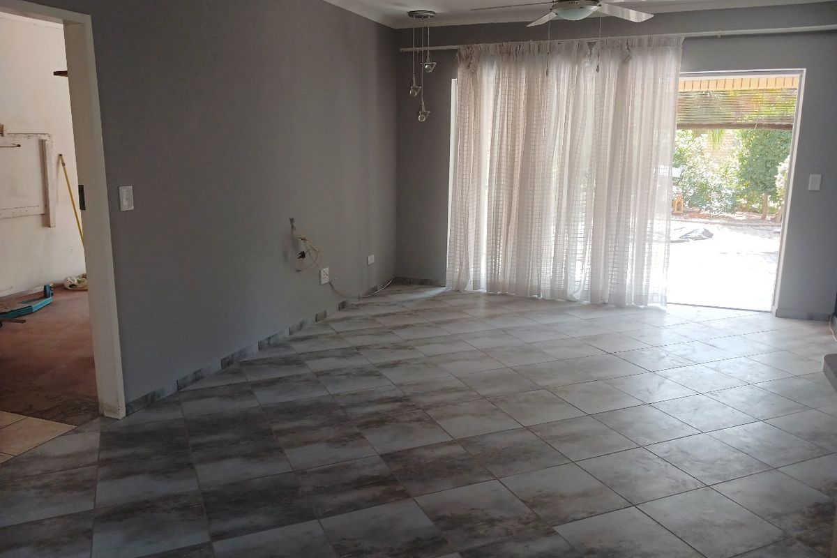 An empty living room featuring tiled flooring, a ceiling fan, and a sliding glass door providing access to the outdoor area.
