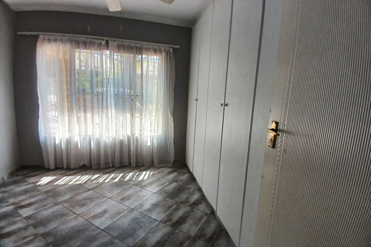 A bright, empty bedroom featuring tiled flooring, built-in cupboards, and a ceiling fan, offering a clean canvas for personalization.