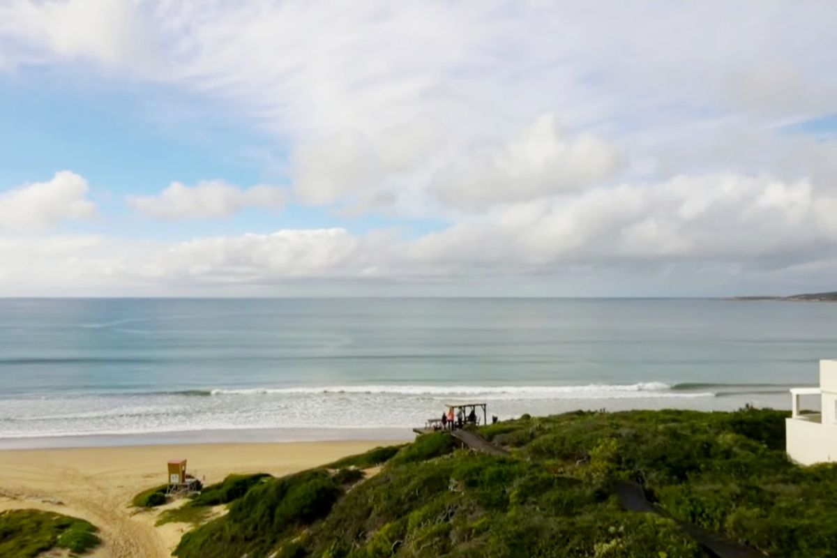 Aerial view of the coastal property featuring direct beach access, natural dune vegetation, and a scenic wooden boardwalk leading to the shoreline.