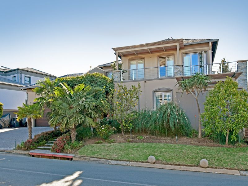A well-maintained double-story residential property featuring a paved driveway, landscaped front garden, and an upper-level balcony with stainless steel railings.