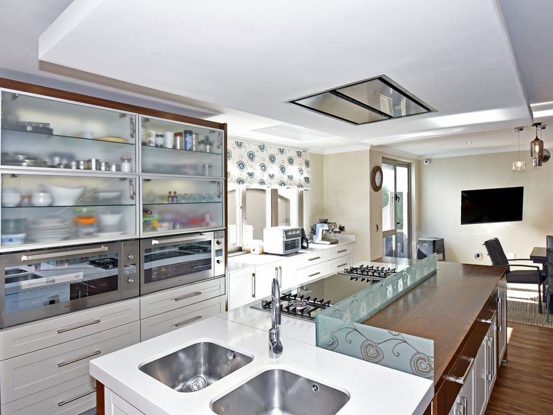 Modern open-plan kitchen featuring a large central island with integrated gas hob, double sink, and ample built-in cabinetry with glass-fronted display units.