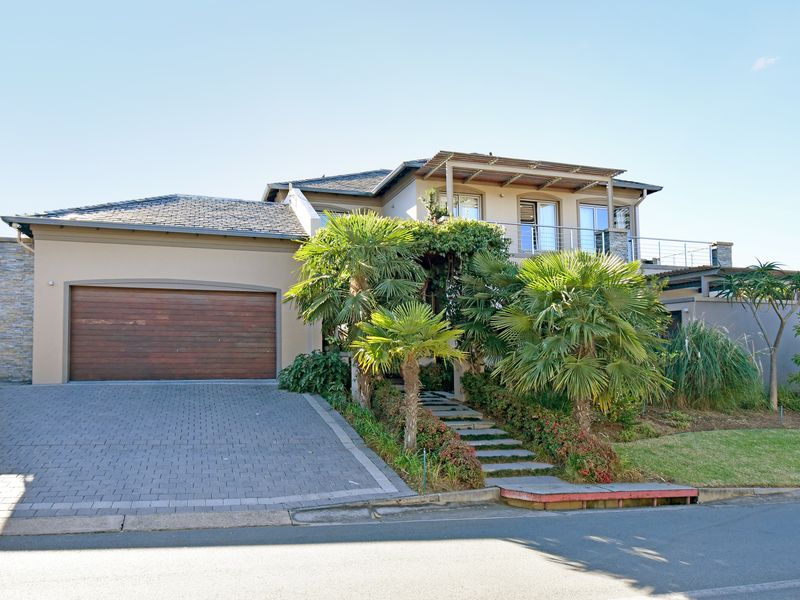 A well-maintained double-story residential property featuring a paved driveway, double garage, landscaped garden with mature palms, and an upper-level balcony.