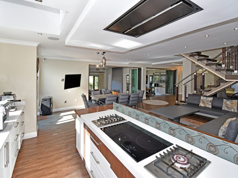 Spacious open-plan kitchen and living area featuring a central island with integrated gas and electric hobs, modern cabinetry, and a floating staircase.