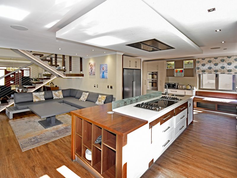 Spacious open-plan living area featuring a modern kitchen with a central island, gas hob, built-in oven, and a contemporary staircase with glass balustrades.