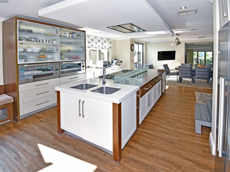 Spacious open-plan kitchen featuring a large central island with dual sinks, integrated appliances, and modern cabinetry, flowing into the dining area.