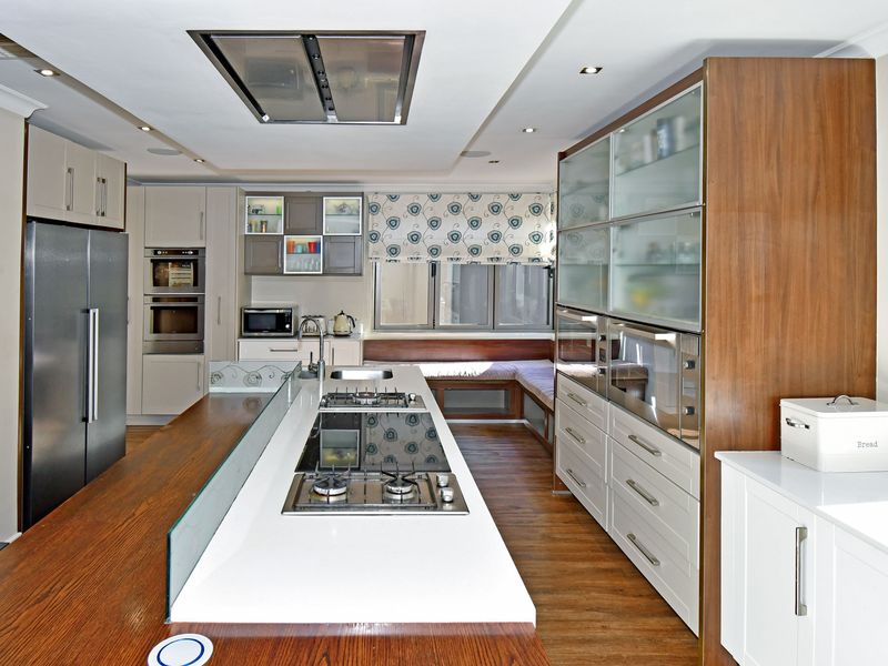 Modern kitchen featuring a large central island with integrated gas hob, built-in wall ovens, ample cabinetry, and a cozy built-in window seating area.