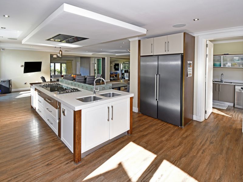 Modern open-plan kitchen featuring a large central island with integrated gas hob, double sink, and adjacent scullery area with ample cabinetry.