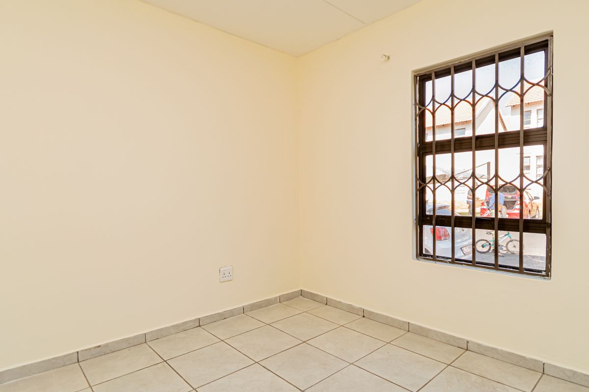 A clean, empty bedroom featuring neutral wall paint, tiled flooring, and a window fitted with security bars.