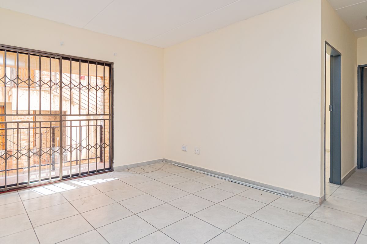 An empty living room featuring tiled flooring, neutral walls, and a sliding door with a security gate leading to an exterior area.