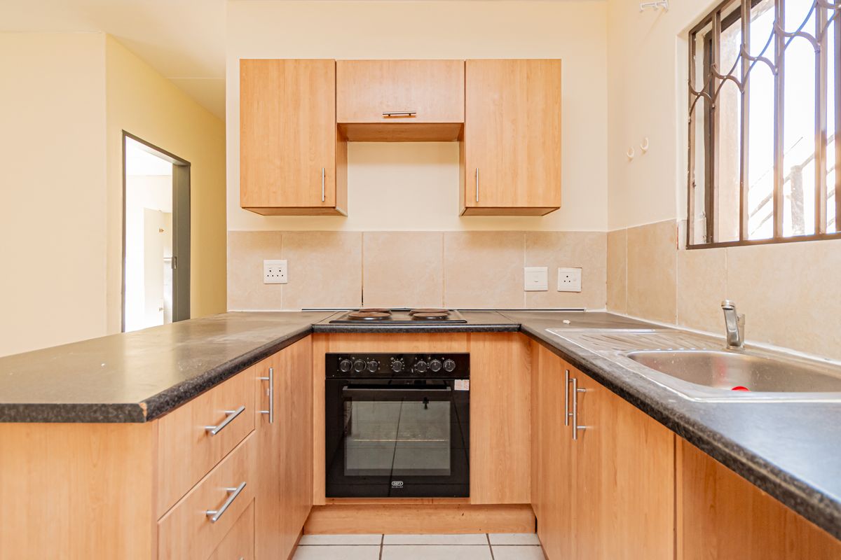 A functional kitchen featuring light wood-finish cabinetry, dark laminate countertops, a built-in oven with hob, and a stainless steel sink.