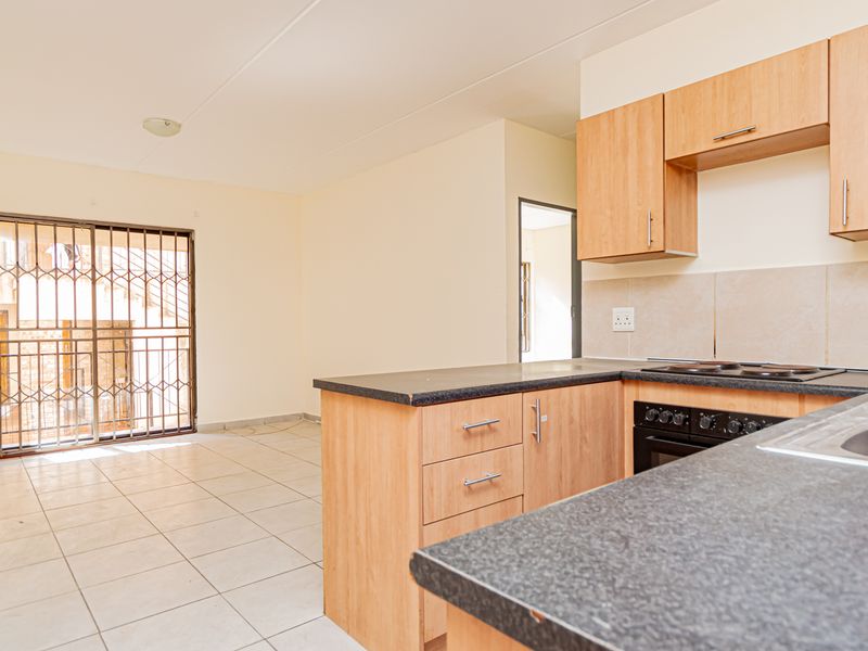 Open-plan kitchen and living area featuring light wood-finish cabinetry, dark countertops, tiled flooring, and a secure sliding door leading to the exterior.