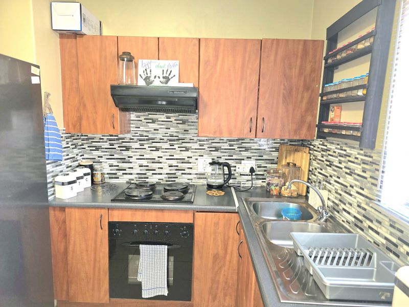 A functional kitchen featuring wood-look cabinetry, a mosaic tile backsplash, a built-in oven with hob, and a double-basin stainless steel sink.