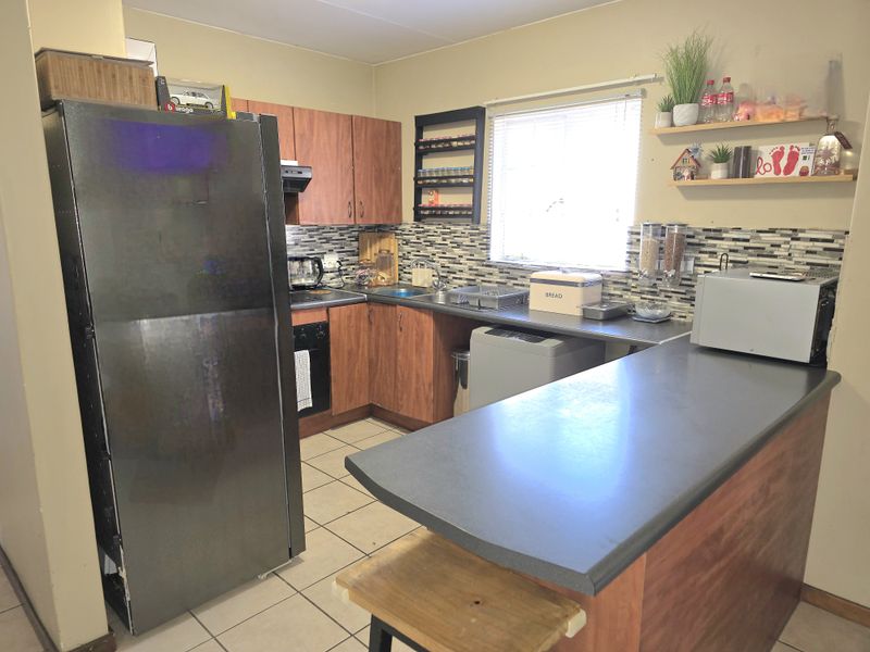 Functional kitchen featuring wood-look cabinetry, mosaic tile backsplash, breakfast bar, and integrated stove with extractor fan.