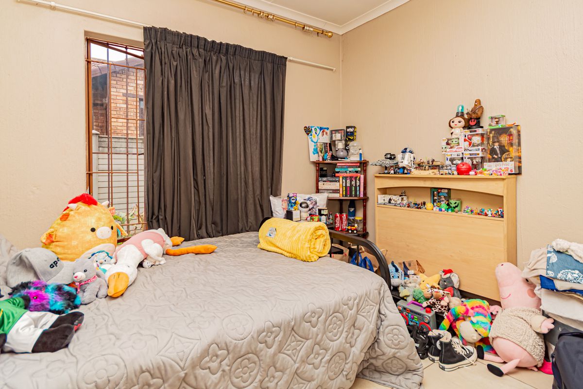 A standard bedroom featuring neutral walls, a window with security bars, and curtain rods, providing a functional space for rest.