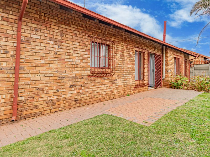 Rear exterior view of the house featuring a face brick facade, paved patio area, and secure window bars leading to a garden.