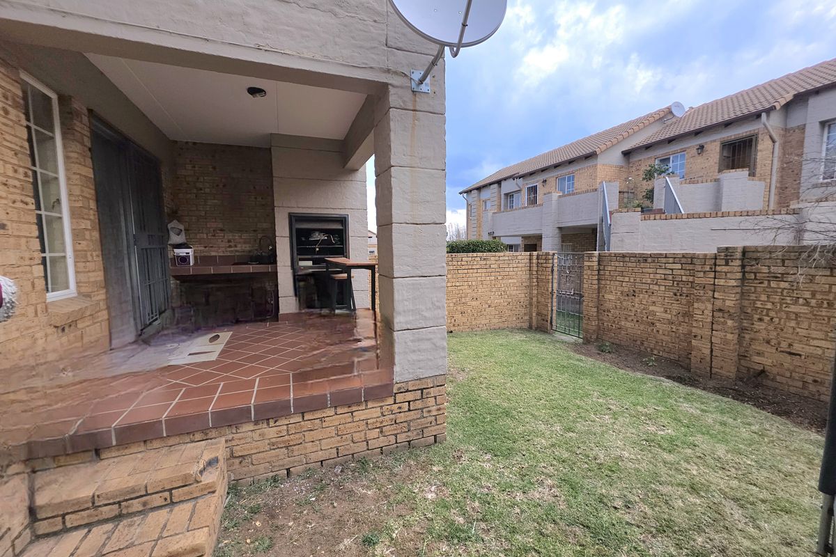 Covered patio area featuring a built-in braai and tiled flooring, leading out to a private garden with perimeter brick walling.