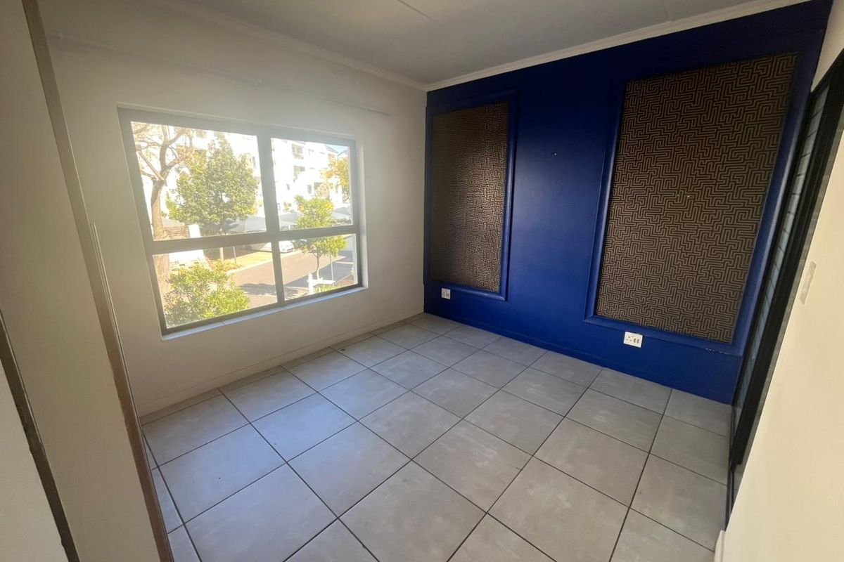 A bright, empty bedroom featuring large windows, tiled flooring, and a bold blue accent wall with decorative panels.