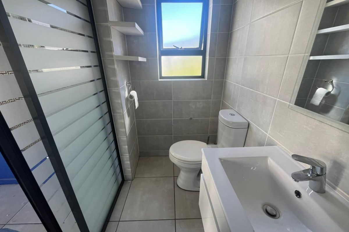 A modern bathroom featuring a vanity with basin, a toilet, and a glass-enclosed shower with neutral wall and floor tiling.