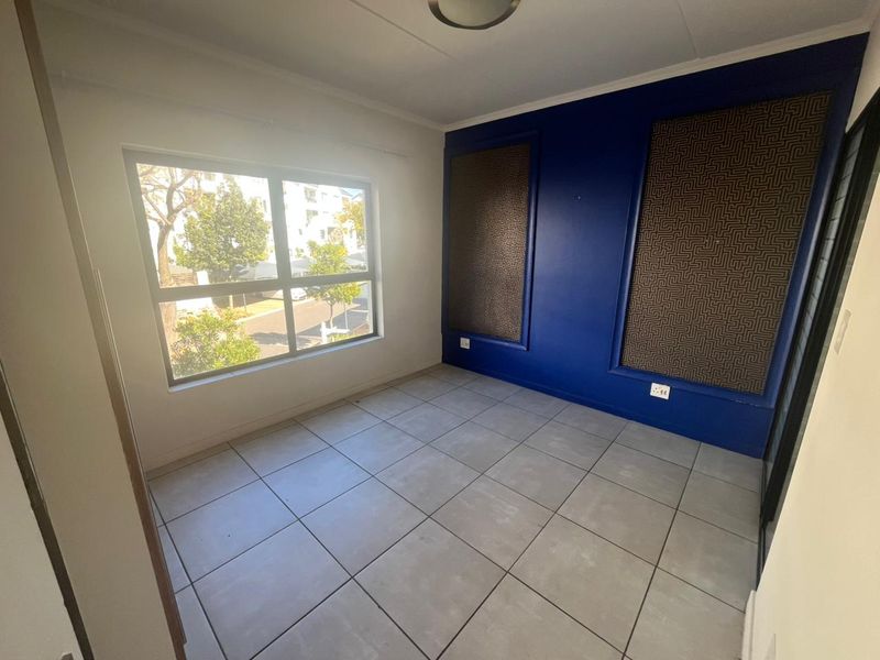 A bright, empty bedroom featuring large windows, tiled flooring, and a bold blue accent wall with decorative panels.