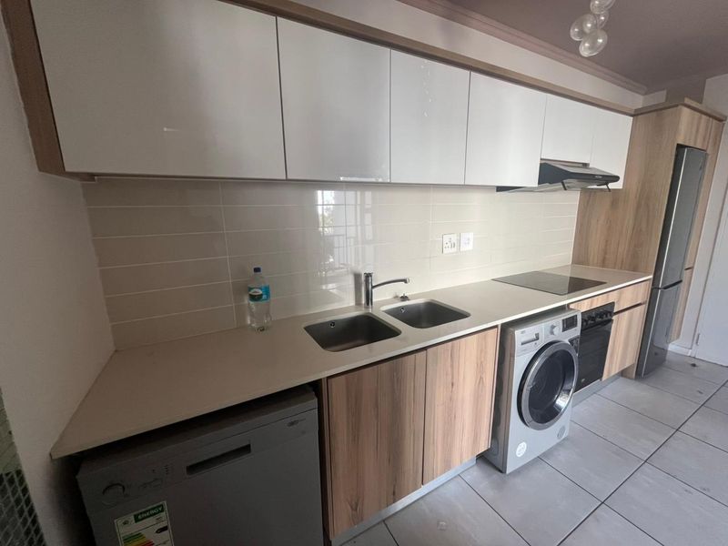 Modern kitchen featuring sleek wood-grain cabinetry, light-toned countertops, integrated stainless steel sink, built-in oven, hob, extractor fan, and space for under-counter appliances.