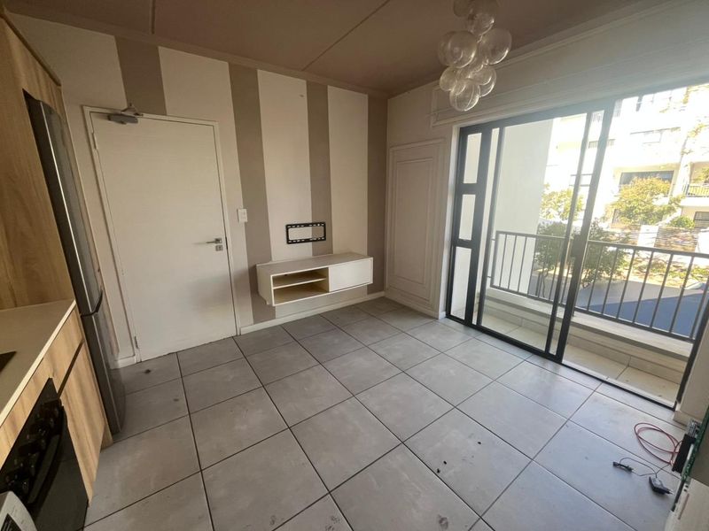 Open-plan living area featuring large format floor tiles, a wall-mounted media console, and sliding glass doors leading to a private balcony.