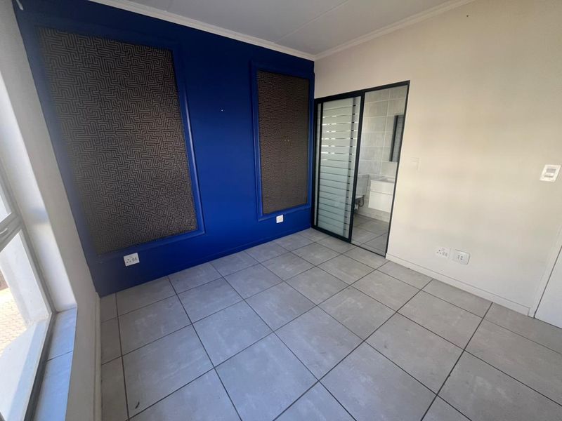 A bedroom featuring tiled flooring, a bold blue accent wall with decorative panels, and an integrated sliding door leading to an en-suite bathroom.