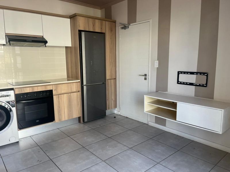 Open-plan kitchen featuring modern wood-grain cabinetry, built-in oven, hob, extractor fan, and tiled flooring, adjacent to a wall-mounted media console.