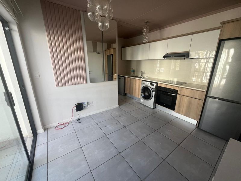 Modern open-plan kitchen featuring light wood-tone cabinetry, white upper cabinets, integrated oven, hob, extractor fan, and tiled flooring with direct access to a balcony.