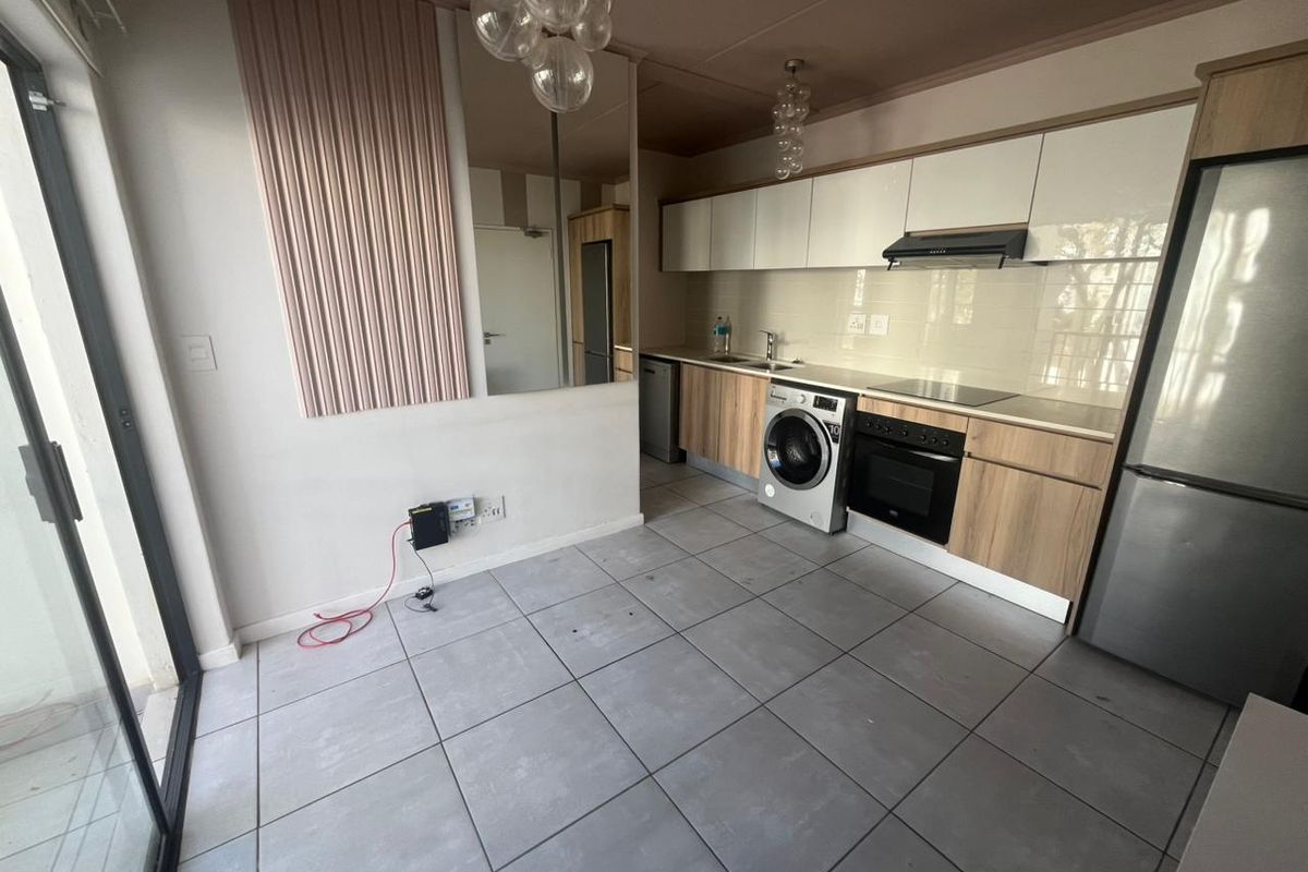 Modern open-plan kitchen featuring light wood-tone cabinetry, white upper cabinets, integrated oven, hob, extractor fan, and tiled flooring with direct access to a balcony.