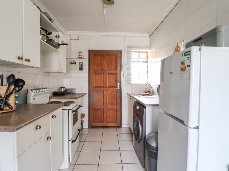 A functional galley-style kitchen featuring tiled flooring, white cabinetry, laminate countertops, and dedicated space for a washing machine and freestanding stove.