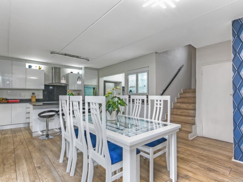 Open-plan kitchen and dining area featuring modern cabinetry, integrated appliances, wood-look flooring, and a staircase leading to the upper level.