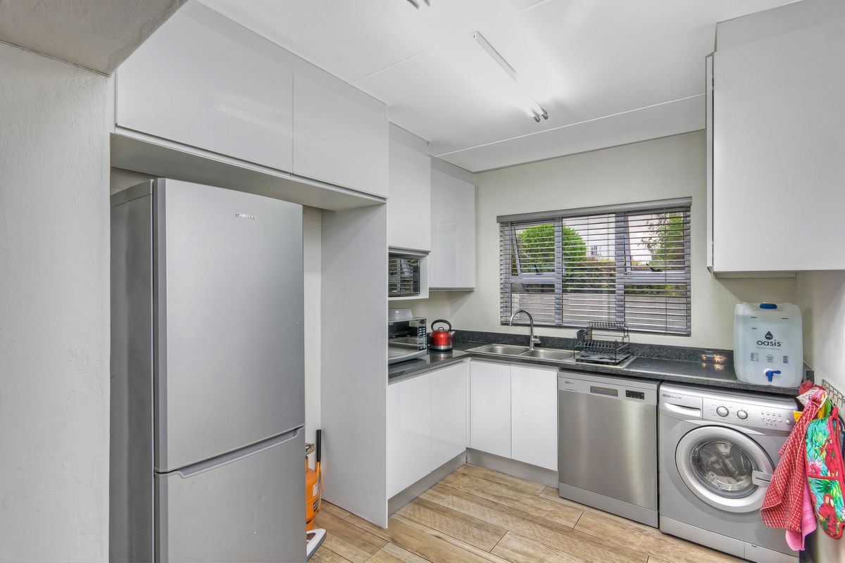 A functional kitchen featuring modern white cabinetry, dark stone countertops, a double sink, and integrated space for laundry appliances.