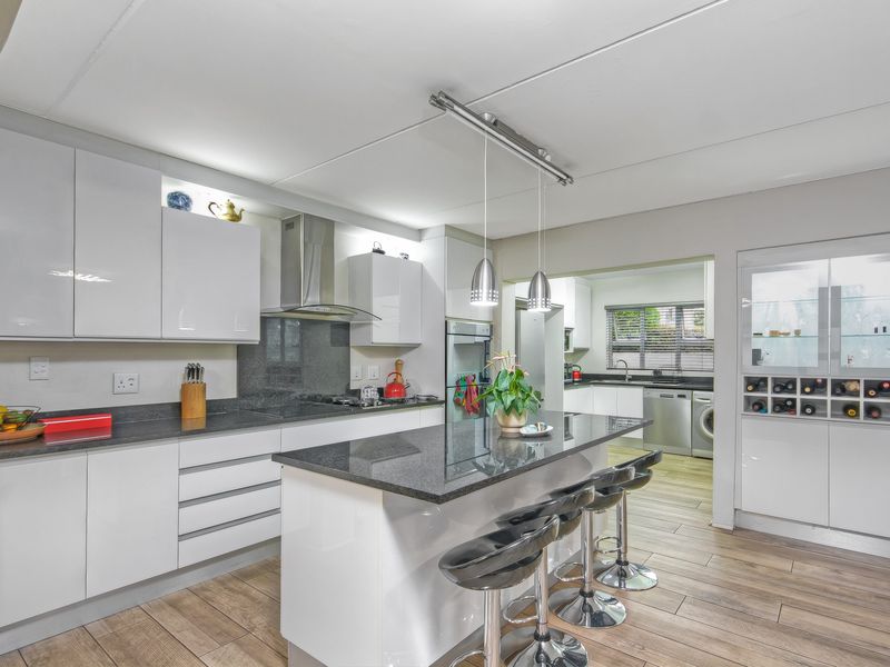 Modern kitchen featuring high-gloss cabinetry, granite countertops, a central island with breakfast bar, and an adjoining scullery area with additional workspace.