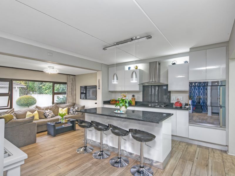 Modern open-plan kitchen featuring a central island with granite countertops, sleek cabinetry, built-in oven, and extractor fan, seamlessly flowing into the adjacent living area.