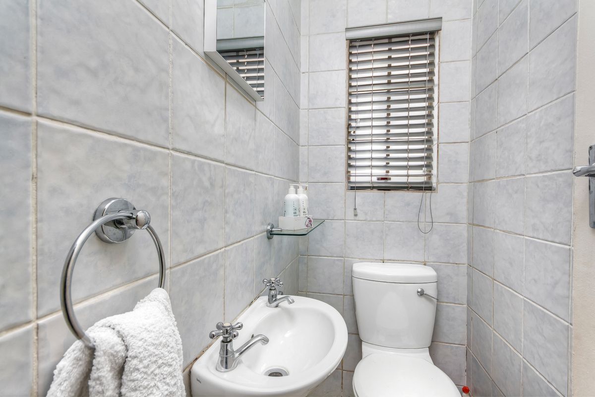 Compact guest bathroom featuring a wall-mounted basin, standard toilet, and full-height wall tiling with a small window for natural light.