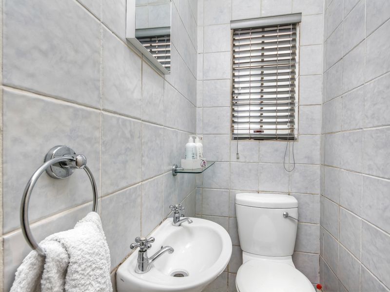 Compact guest bathroom featuring a wall-mounted basin, standard toilet, and full-height wall tiling with a small window for natural light.