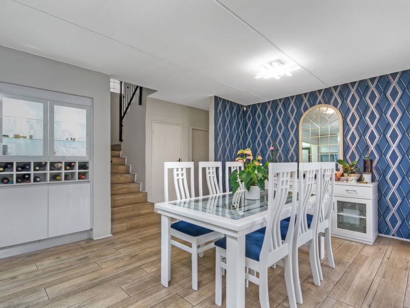 Dining area featuring wood-look tile flooring, a built-in wine storage cabinet, and a decorative feature wall with staircase access.