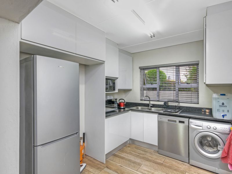 A functional kitchen featuring modern white cabinetry, dark stone countertops, a double sink, and integrated space for laundry appliances.