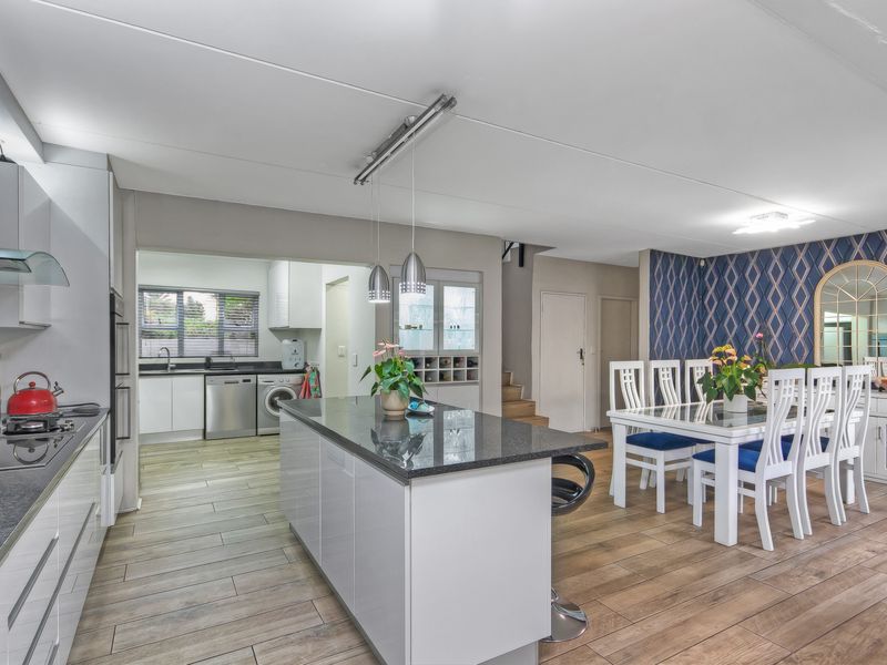 Modern open-plan kitchen and dining area featuring a central island, sleek cabinetry, integrated appliances, and wood-look tiled flooring.