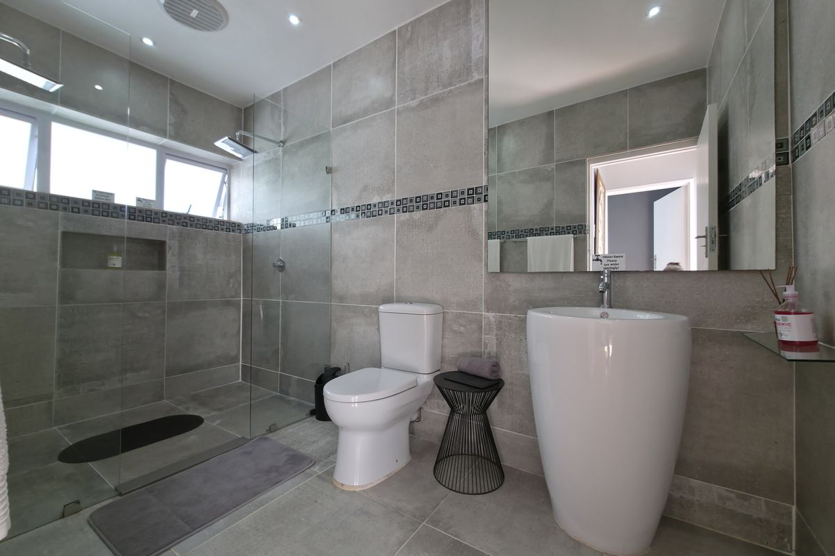 Modern bathroom featuring a walk-in glass shower, pedestal basin, wall-mounted mirror, and neutral floor-to-ceiling tiling.
