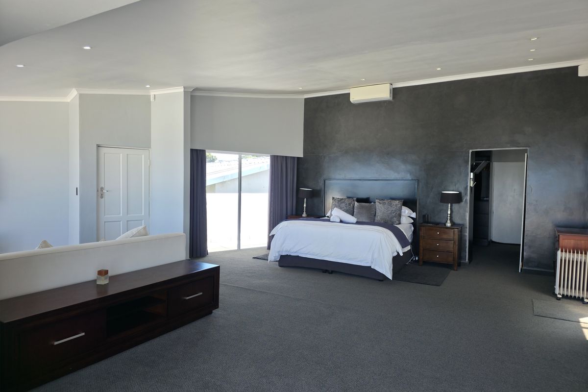 Spacious bedroom featuring a dark feature wall, recessed ceiling lighting, wall-mounted air conditioning unit, and sliding glass doors leading to an outdoor area.