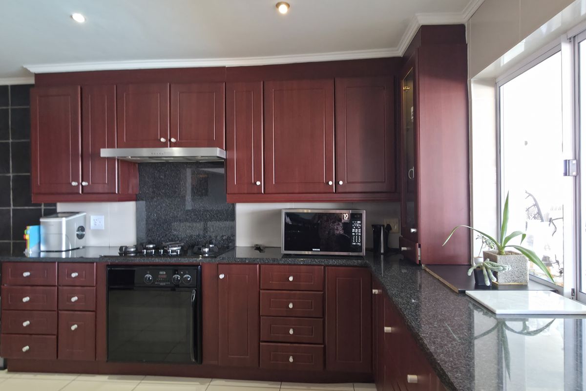 A well-maintained kitchen featuring dark wood cabinetry, granite countertops, a built-in oven, gas hob, and stainless steel extractor fan.