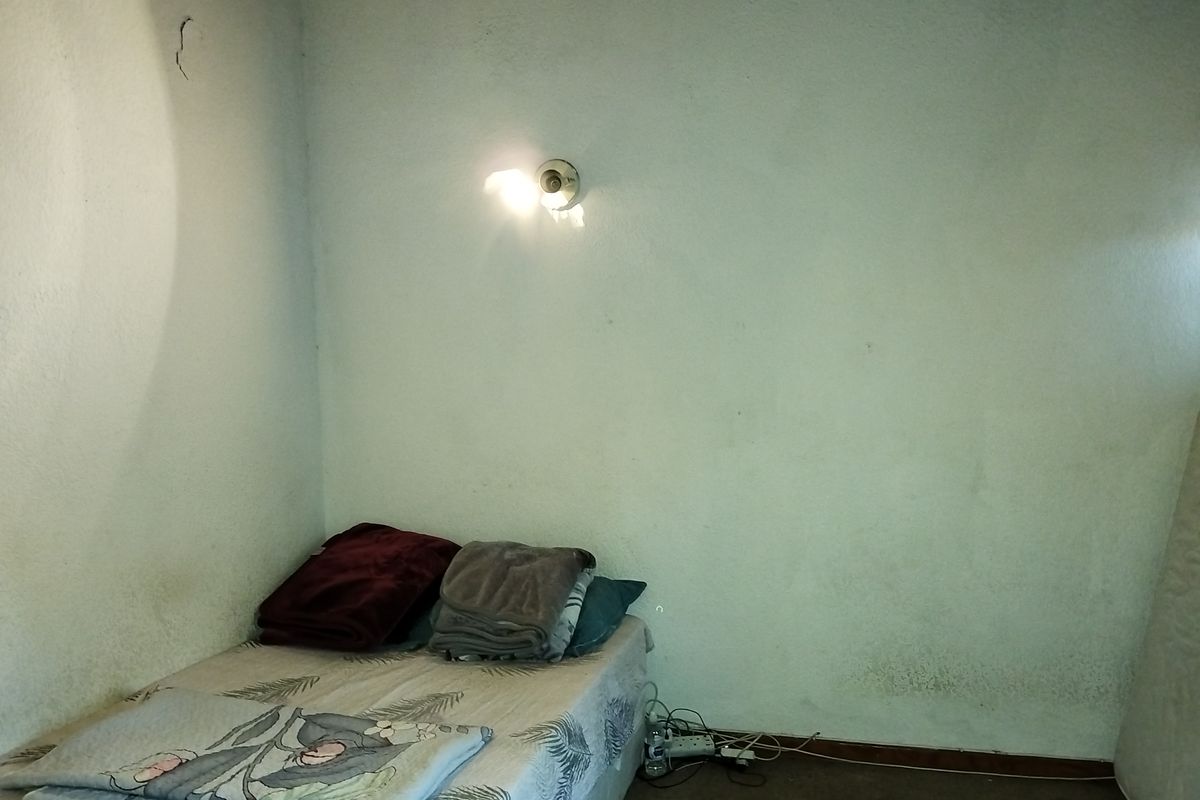 A bedroom featuring a wall-mounted light fixture, showing signs of wear including wall cracks and surface staining.