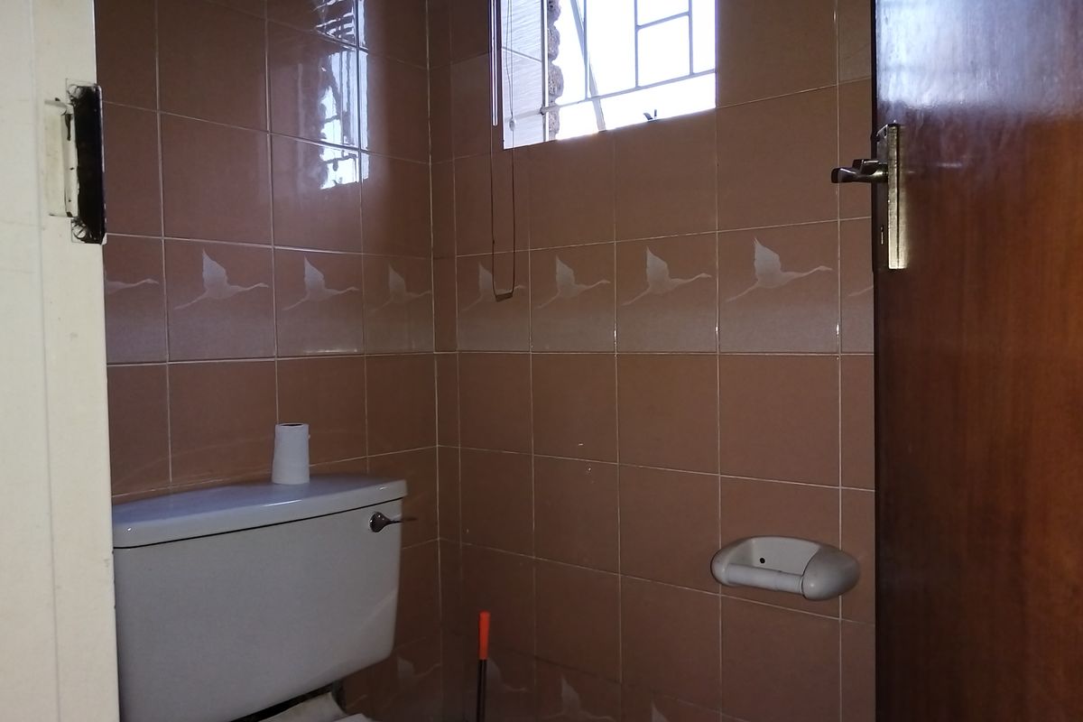 A compact bathroom featuring dated ceramic wall tiles with decorative motifs, a standard toilet, and a window with security bars.