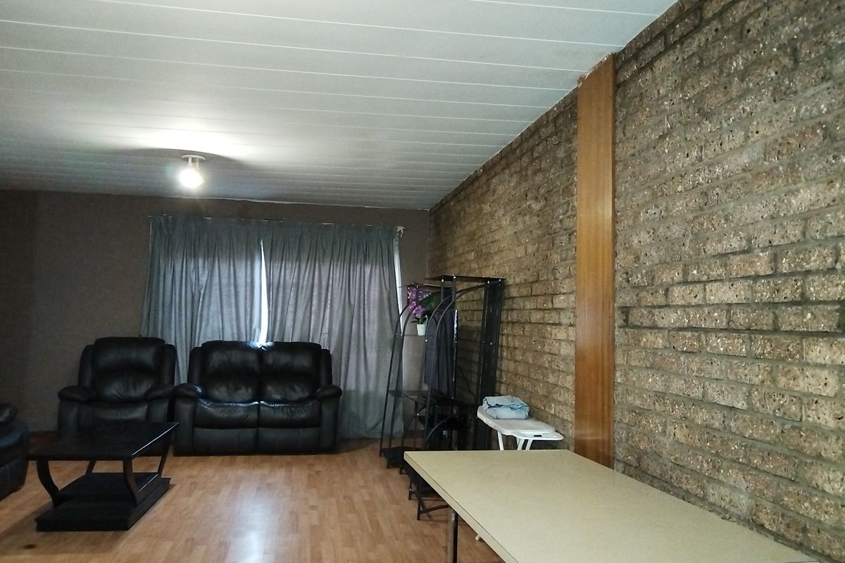 Living room featuring an exposed brick feature wall, laminate flooring, and a panelled ceiling.