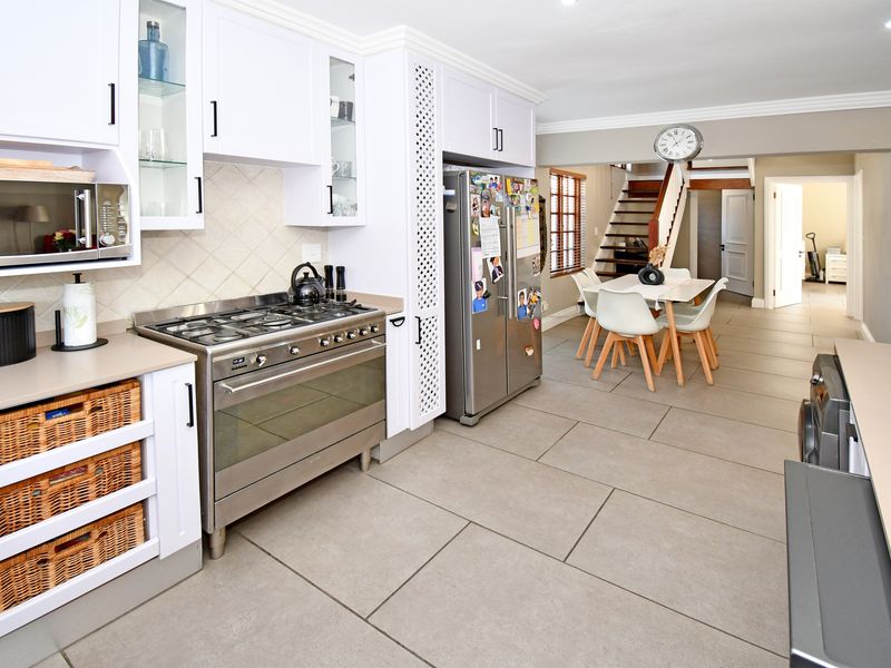 Open-plan kitchen and dining area featuring modern white cabinetry, a stainless steel gas stove, and large format floor tiles leading to a staircase.