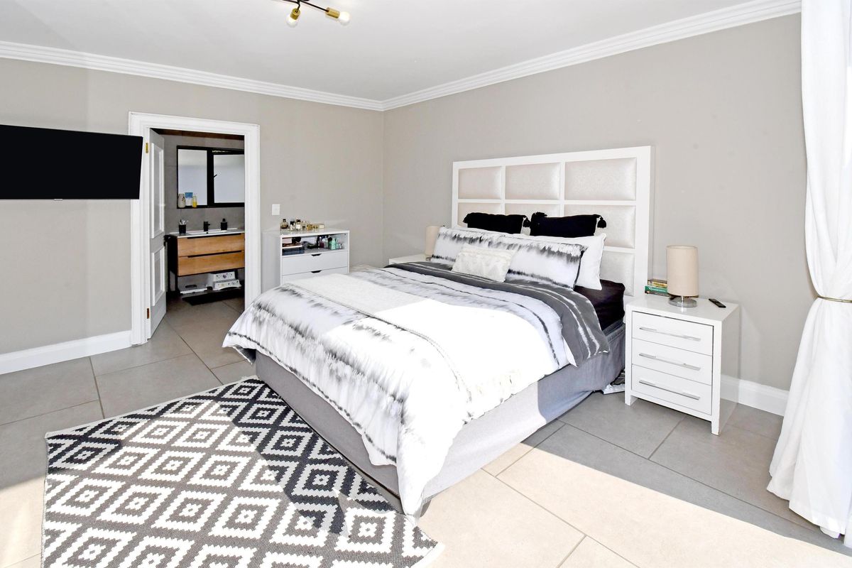 Spacious bedroom featuring neutral wall tones, tiled flooring, crown molding, and direct access to an en-suite bathroom.