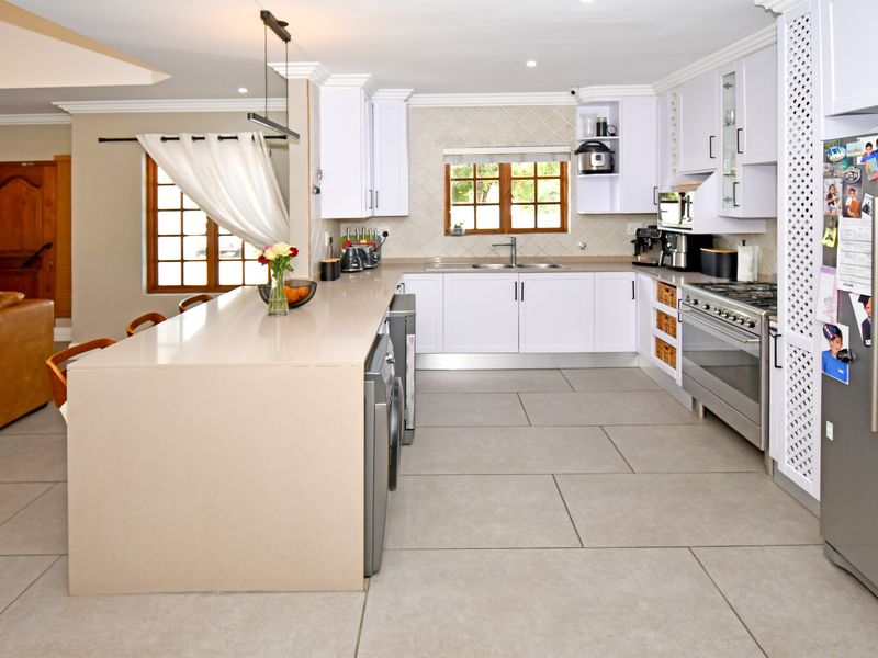 Modern kitchen featuring a large central island, quartz countertops, white cabinetry, stainless steel appliances, and neutral large-format floor tiles.