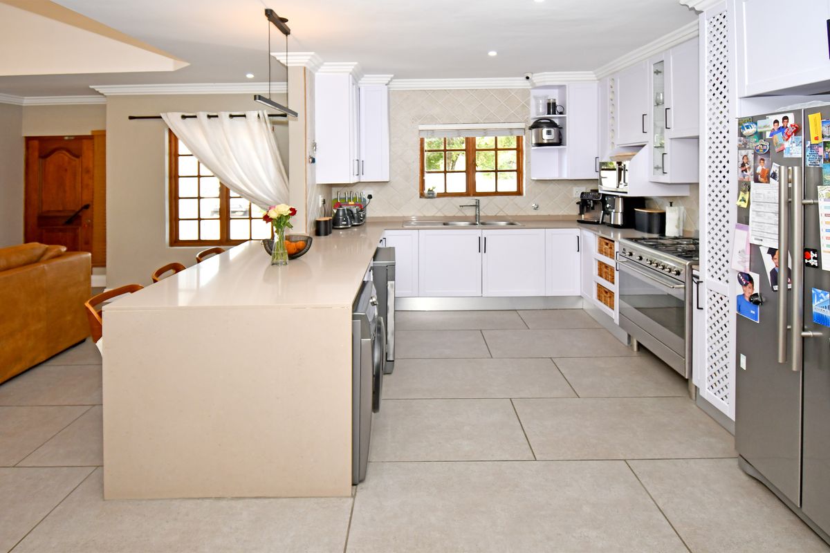 Modern kitchen featuring a large central island, quartz countertops, white cabinetry, stainless steel appliances, and neutral large-format floor tiles.